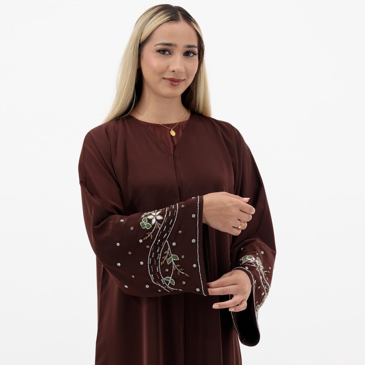 Reema Abaya available in Black, Vanilla, and Chocolate Brown with golden and silver beaded sleeves in a floral and leafy design. Made from crepe fabric with popper buttons, available in sizes 50-60. Includes a matching hijab.